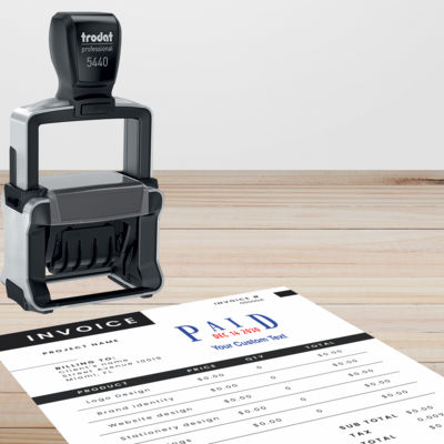 picture of a Trodat Professional Date Stamp on wood table with a paper invoice stamped with 'PAID Date' in blue and redf